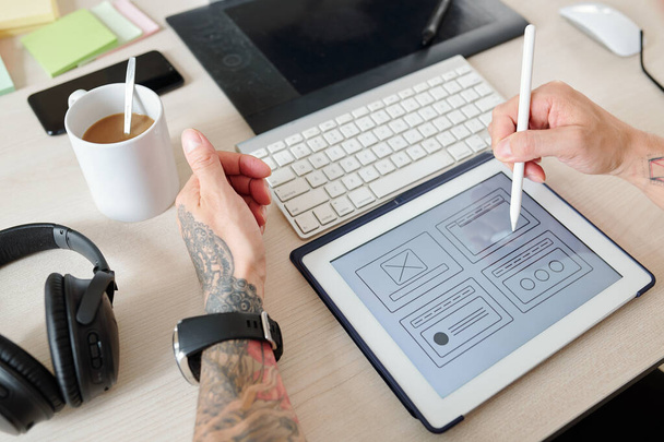 Handen van UI ontwerper werken op de interface van nieuwe website of mobiele applicatie, hij wijst naar tablet computer met digitale pen - Foto, afbeelding