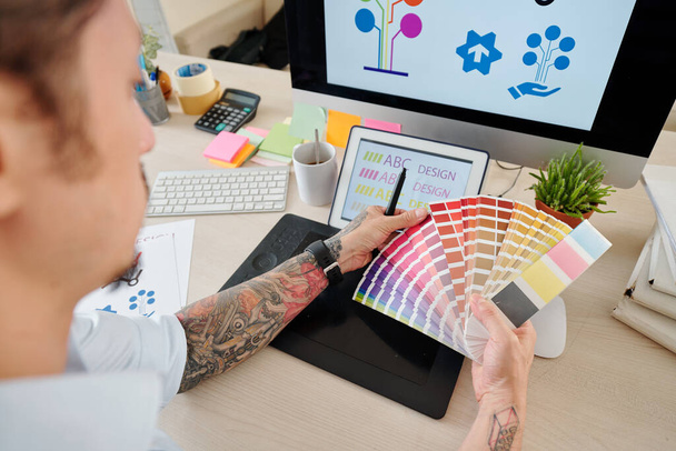 Hands of graphic designer κοιτάζοντας την παλέτα και επιλέγοντας χρώμα για τα λογότυπα της εταιρείας - Φωτογραφία, εικόνα