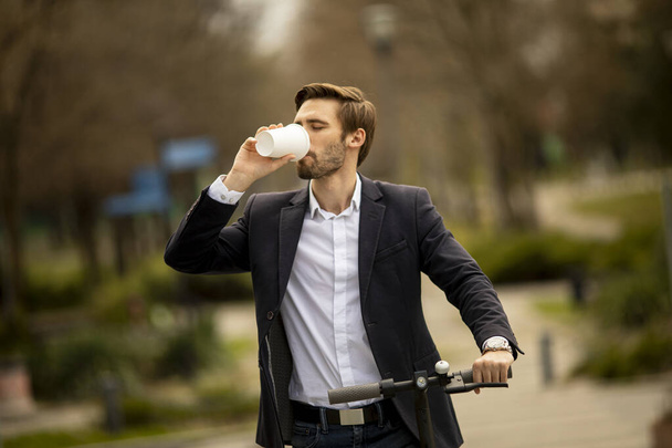 Bonito jovem empresário com tirar xícara de café em scooter elétrico - Foto, Imagem