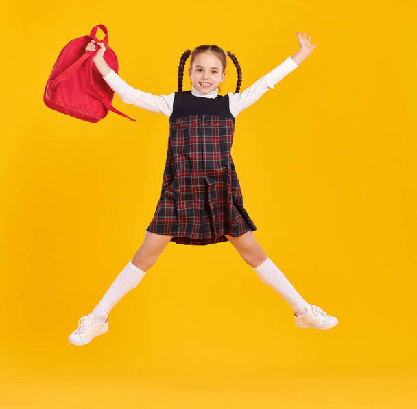 Plná délka dívka v módní školní uniformě držení taška a skákání na žlutém pozadí - Fotografie, Obrázek