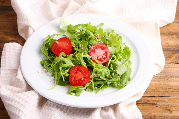 Green salad made with  arugula, tomatoes and sesame  on plate, on wooden background - Foto, Bild