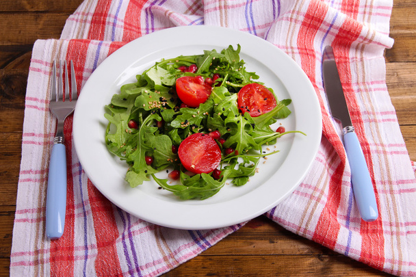 Green salad made with  arugula, tomatoes and sesame  on plate, on wooden background - Foto, Imagem