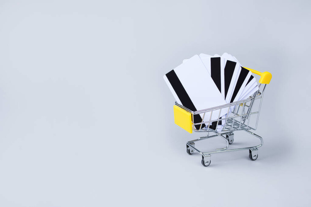 Žlutý nákupní košík s kreditními kartami uvnitř na světle šedém pozadí s kopírovacím prostorem pro text. Prodejní akce, Černý pátek a Kybernetické pondělí koncept v barvách roku 2021, selektivní zaměření - Fotografie, Obrázek