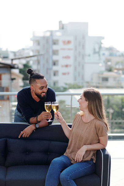 Улыбающиеся юноша и девушка пьют шампанское и флиртуют на вечеринке на крыше - Фото, изображение