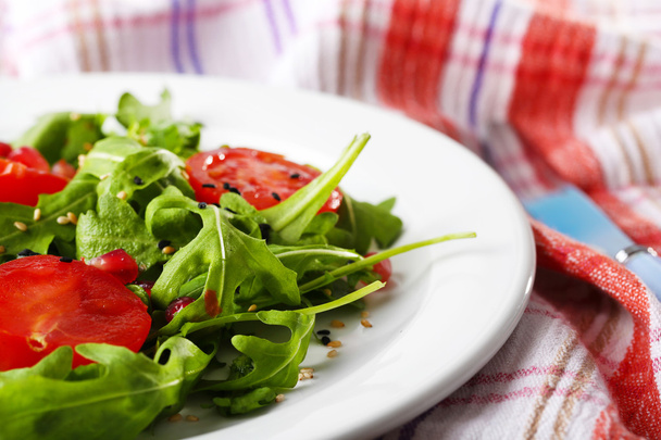Green salad made with  arugula, tomatoes and sesame  on plate, on wooden background - Zdjęcie, obraz