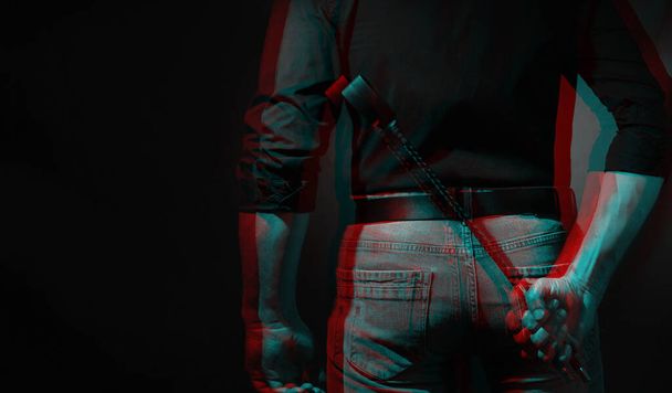 a sexy man holds a bdsm whip on a red background behind his back. Black and white with 3D glitch virtual reality effect - Photo, Image