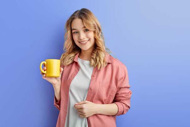 Симпатичная позитивная девушка пьет кофе или чай утром перед школой или университетом - Фото, изображение