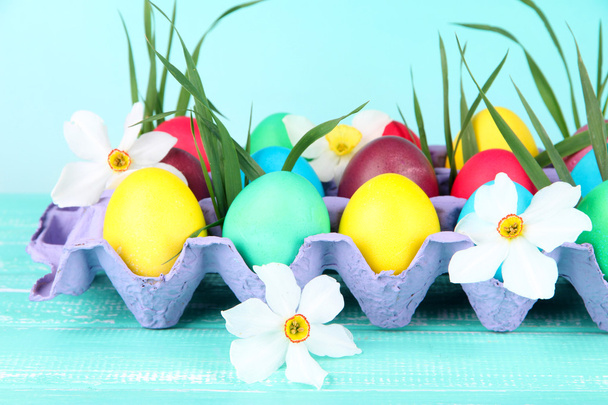 barevné velikonoční vajíčka s trávou a květinami v zásobníku na stole na světlé pozadí - Fotografie, Obrázek