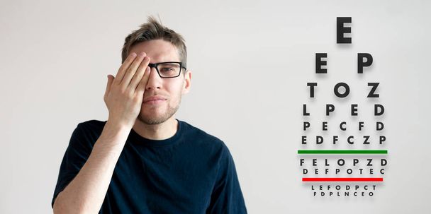 молодой человек проверить зрение, изучить здоровье с тестовыми буквами диаграммы - Фото, изображение