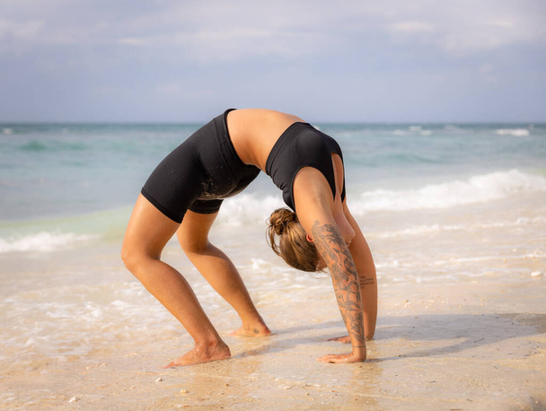 Beach yoga. Young woman practicing Chakrasana or Urdhva Dhanurasana, Full Wheel Pose. Upward facing bow pose is a deep backbend. Flexibility, strength, patience. Thomas beach, Bali, Indonesia - 写真・画像