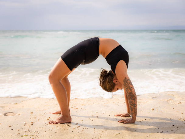 Strand yoga. Jonge vrouw die Chakrasana of Urdhva Dhanurasana beoefent, Full Wheel Pose. Naar boven gerichte boeg houding is een diepe rugbuiging. Flexibiliteit, kracht, geduld. Thomas strand, Bali, Indonesië - Foto, afbeelding