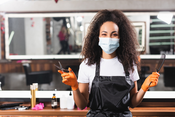 保護マスク保持はさみや櫛でアフリカ系アメリカ人の美容師  - 写真・画像