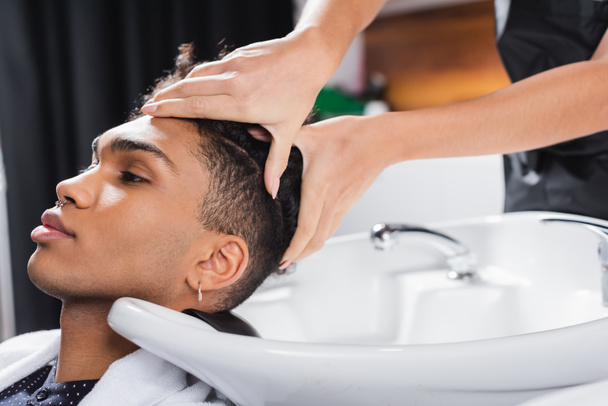 tête de lavage coiffeur de client afro-américain près de l'évier dans le salon  - Photo, image