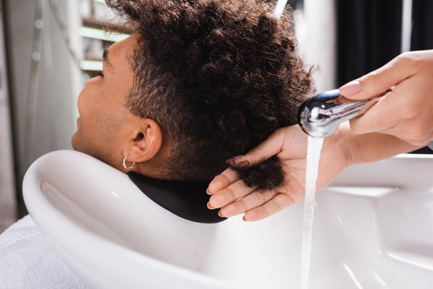 African american man sitting near hairdresser with shower in salon  - 写真・画像