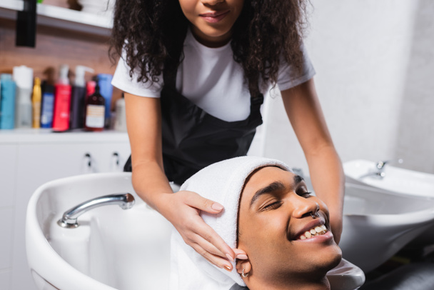 Coiffeur afro-américain enveloppant la tête du client souriant dans une serviette  - Photo, image