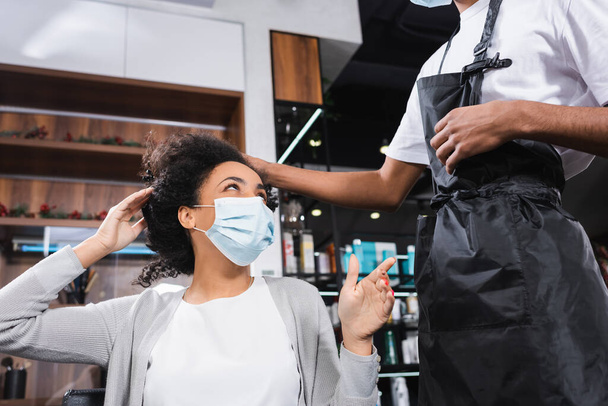 African american woman in protective mask pointing at hairstylist  - Φωτογραφία, εικόνα