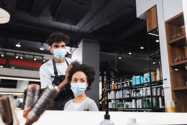African american hairstylist touching hair of woman in medical mask  - Photo, Image