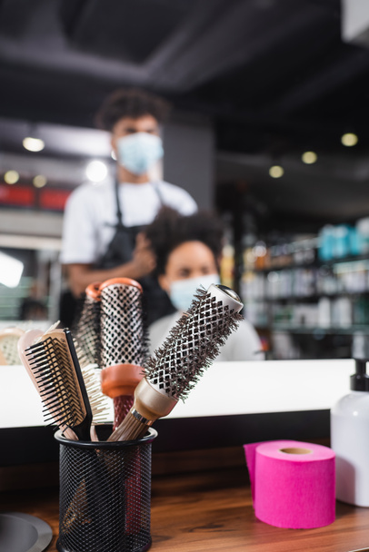 Haarbürsten und Kragenpapier in Spiegelnähe und verschwommener Friseur bei der Arbeit mit Kunden  - Foto, Bild