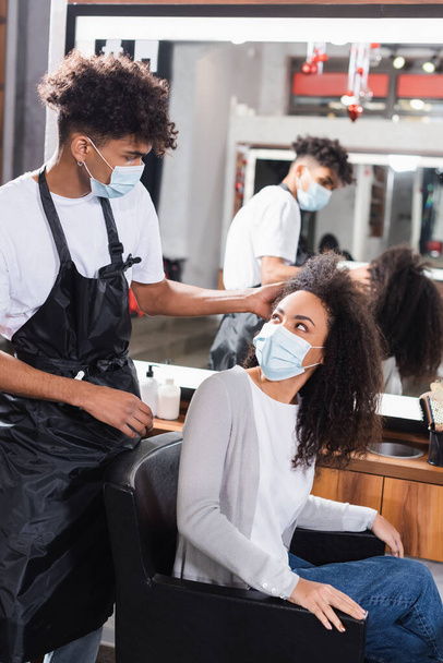 Afričanky americká kadeřnice dotýká kudrnaté vlasy ženy v křesle v salonu  - Fotografie, Obrázek