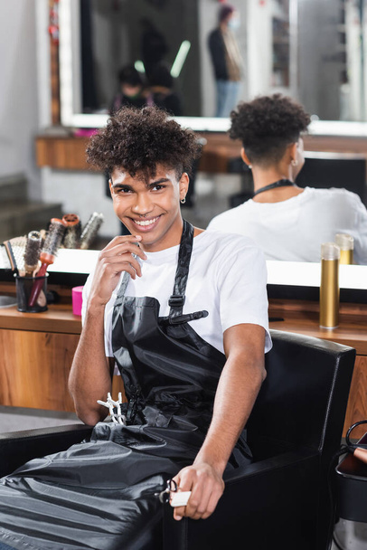 African american hairdresser with comb and scissors on blurred foreground smiling  - Фото, зображення