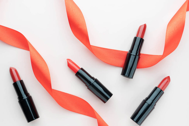 Luxe rode lippenstiften van verschillende tinten in zwarte buisverpakking met versierd lint op beige ondergrond. Make-up en cosmetica model product concept. Vlakke indeling. - Foto, afbeelding