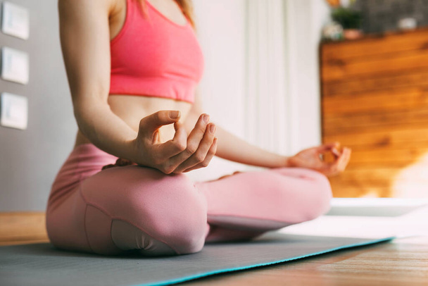 A young woman sits in the lotus position and meditates at home or in a yoga class and meditates. Healthy lifestyle, yoga, meditation - Photo, Image