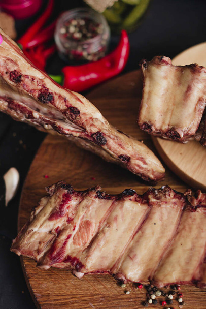 Costillas de cerdo ahumadas con pimiento rojo y especias en una tabla de madera sobre un fondo negro. - Foto, imagen