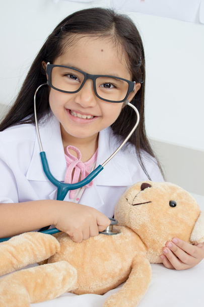 Азиатка играет в доктора со стетоскопом и медвежьей куклой
 - Фото, изображение