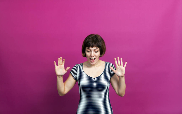 Woman with short hair raising   hands and looking down in surpris on   pink background  - Photo, Image