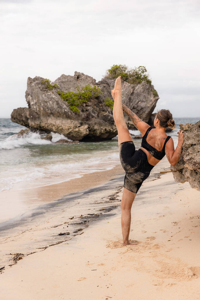 Yoga practice. Caucasian woman practicing Samsahate Hanumanasana, Standing Split Pose. Hamstrings stretching. Flexible body. Yoga retreat. View from back. Thomas beach, Bali, Indonesia - Photo, Image