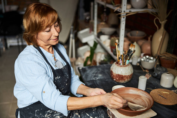 Affascinante donna anziana ceramista pittura ciotola di argilla in laboratorio - Foto, immagini