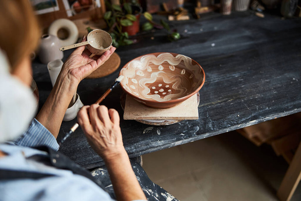 Female potter hands painting on bowl in pottery workshop - Photo, Image