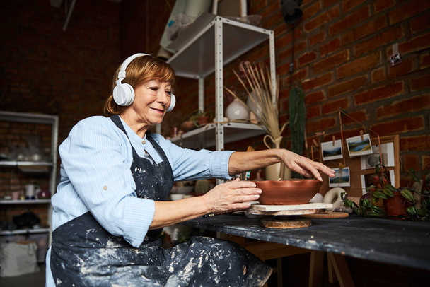 Kobieta garncarka w słuchawkach pracujących w pracowni ceramiki artystycznej - Zdjęcie, obraz