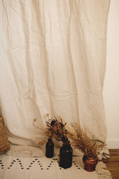 Trockene Protea-Blume in der Vase, Pampasgras auf Boho-Teppich auf beigem Leinentuch. Atmosphärisch unkonventionellen Stil Zimmer Details. Boho Dekor für Hochzeit oder im Studio - Foto, Bild
