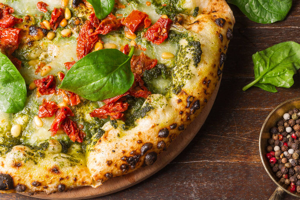 Pala terveellistä kotitekoista pizzaa pinaatilla, aurinkokuivatuilla tomaateilla ja pinjansiemenillä. Makrokehys, vaakasuora - Valokuva, kuva