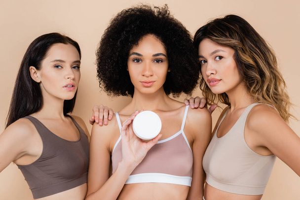 young african american woman showing cosmetic cream near multicultural friends on beige - Foto, Bild