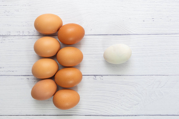 Un huevo blanco dentro de muchos huevos sobre fondo de madera de mesa blanca. huevo de gallina dentro de huevo de pato o diferente humano en el concepto de negocio social o diferente. Enfoques selectivos.Concepto de Vida Solitaria. - Foto, imagen