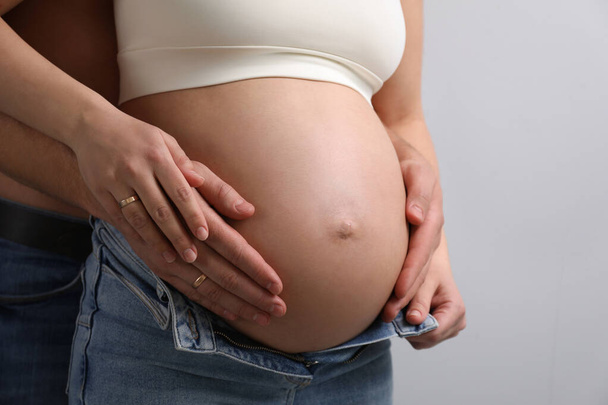 Man touching his pregnant wife's belly on light background, closeup - Foto, Bild