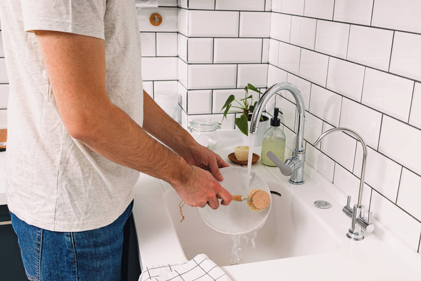 A man washes dishes in the kitchen with a wooden eco brush - Foto, Bild