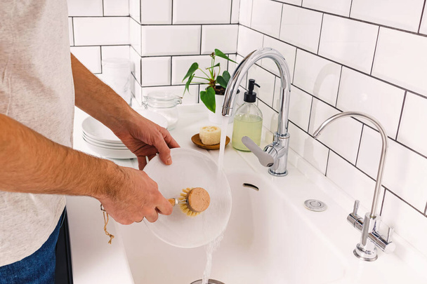 A man washes dishes in the kitchen with a wooden eco brush - Foto, Bild
