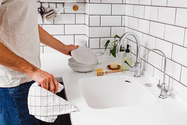 Egy férfi törölje le egy törölköző edények a konyhában fehér csempe. - Fotó, kép