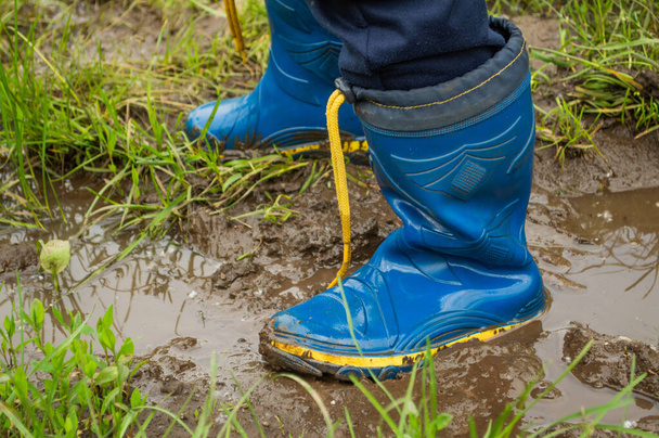Θολή εικόνα του περπατήματος σε λαστιχένιες μπότες μέσα από λακκούβες και λάσπη μετά τη βροχή.. - Φωτογραφία, εικόνα