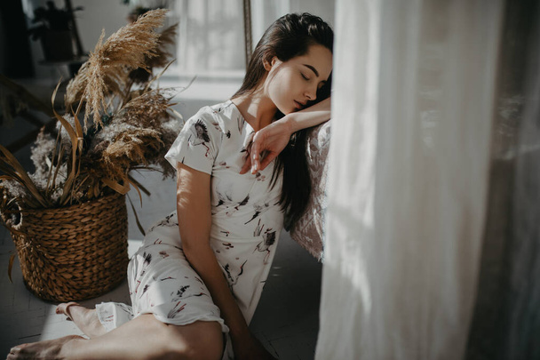 Молода жінка сидить на підлозі і спить на тлі плетеного кошика з сухоцвітами
. - Фото, зображення