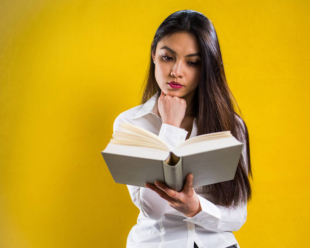 Young woman reading a book - studio shot against yellow background - Foto, Imagen