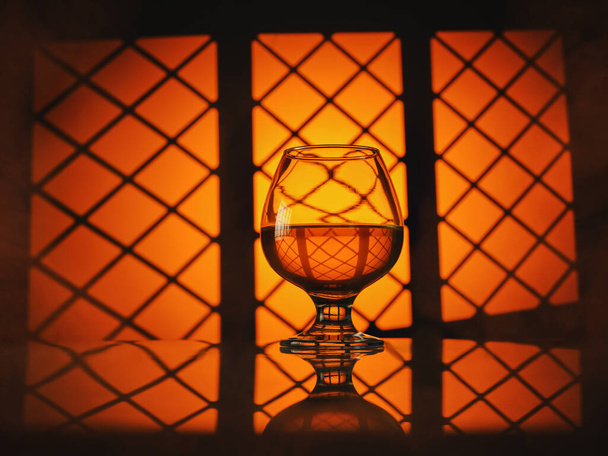 Glass of cognac (whiskey) on a warm orange background - Фото, изображение
