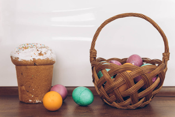 Uova di Pasqua e torta di Pasqua in un cesto. Torta di Pasqua su un tavolo di legno e un cesto di Pasqua con uova gialle, verdi e viola. - Foto, immagini