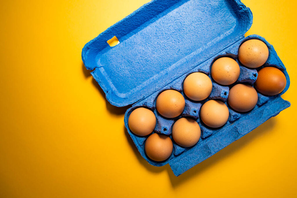 Fresh eggs in and out of blue carton box isolated on yellow background - Φωτογραφία, εικόνα