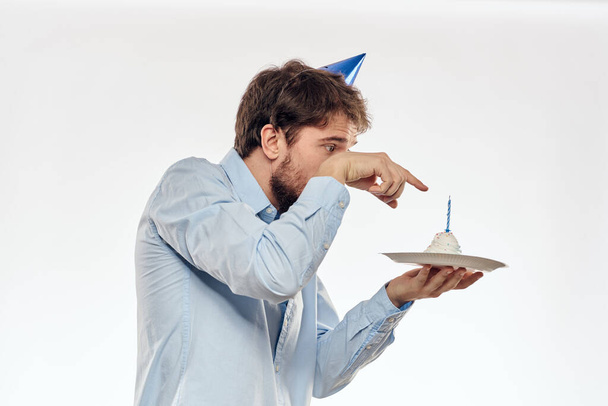 Muž slaví narozeniny na světlém pozadí s dort v talíř flétna zábavná čepice - Fotografie, Obrázek