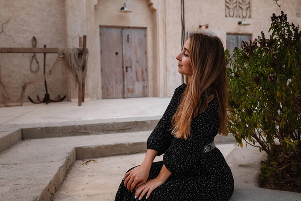 Šťastná žena cestovatel v černých šatech procházky ulicemi starého arabského města nebo vesnice uprostřed pouště. Koncept cestovního ruchu a dobrodružství v Al Seef Dubaj - Fotografie, Obrázek