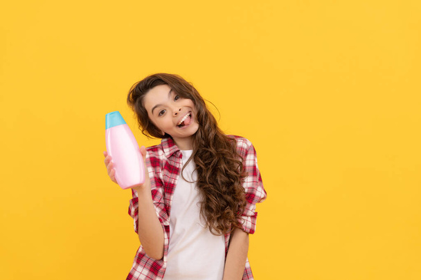 child with conditioner. long curly hair. daily habits and personal care. presenting cosmetic product. beauty. kid use shower gel. happy teen girl with shampoo bottle. shampooing hair in salon. - Photo, Image